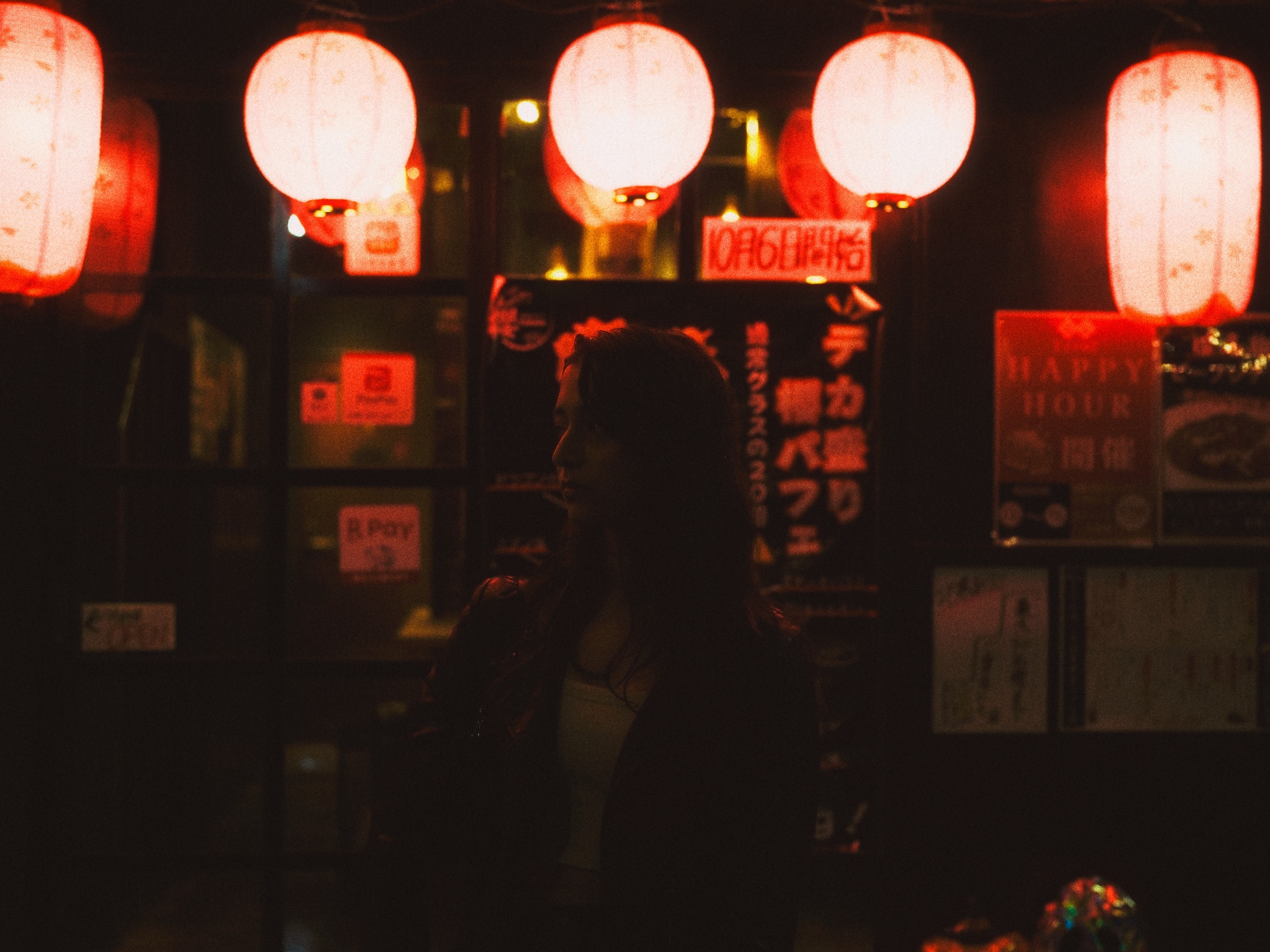 A silhouette beneath red lanterns, waiting for the night to begin.