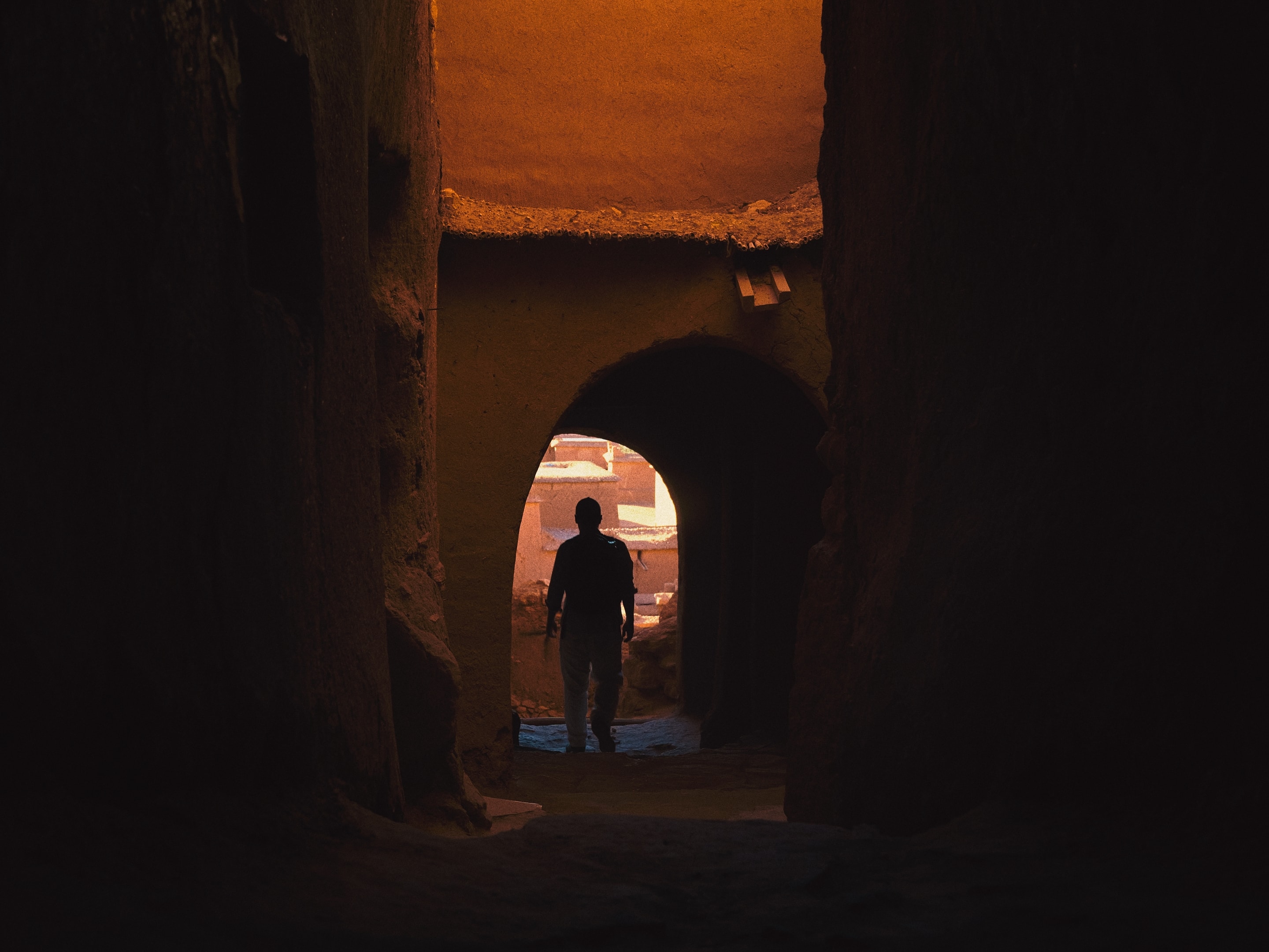 A figure passes beneath sunlit clay walls.